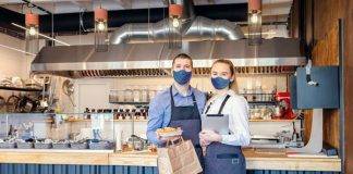 Restaurant workers standing in front of a counter, holding a takeout container and a menu..
