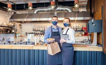 Restaurant workers standing in front of a counter, holding a takeout container and a menu..